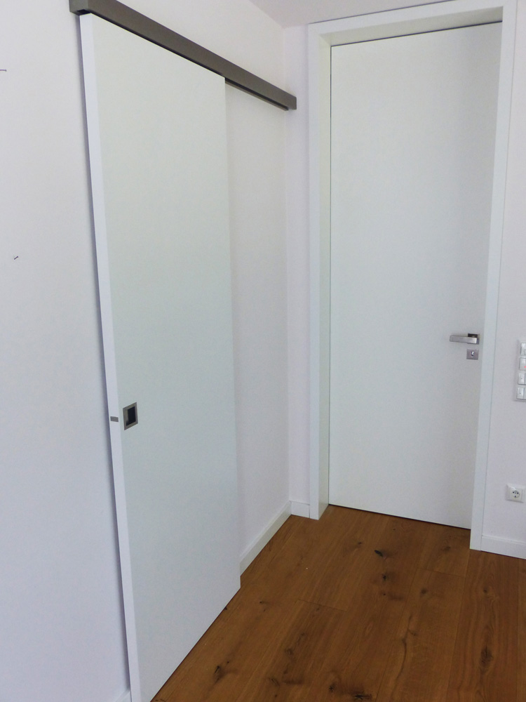 Zwei Türen nebeneinander: weiße Schiebetür und geschlossene Weißlacktür, die jeweils in andere Räume führen