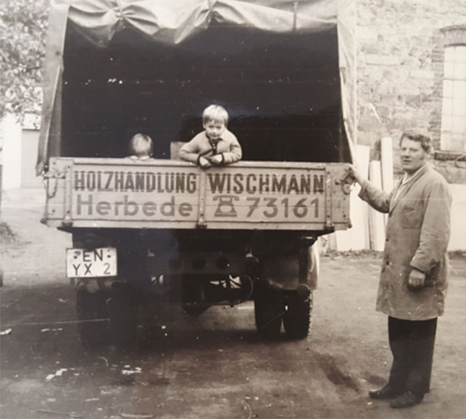 Ein altes vergilbtes Foto eines LKW-Trucks auf dessen Ladefläche zwei kleine Kinder stehen, der Vater daneben