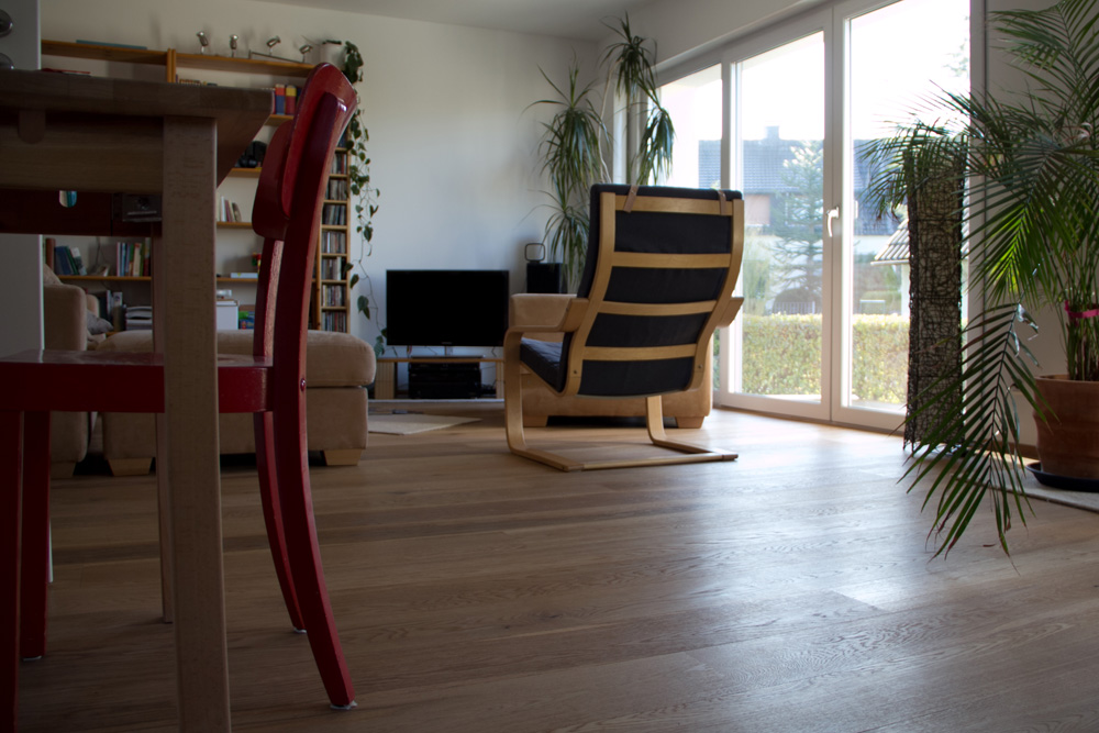 Im Wohnzimmer eines Einfamilienhauses wurde Parkett im Stile der Landhausdiele verlegt, Blick auf Ferneseher und Sofa