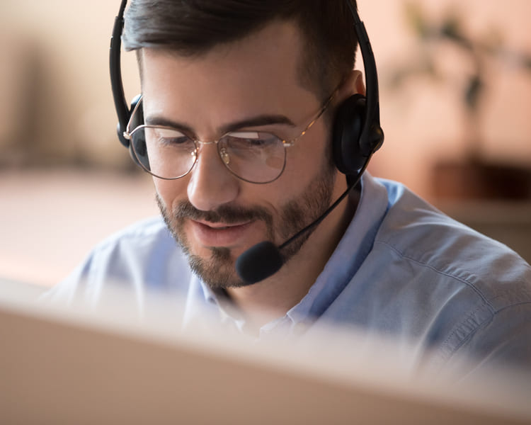 Ein freundlicher Mann mit Headset auf dem Kopf schaut lächelnd und konzentriert auf einen Monitor