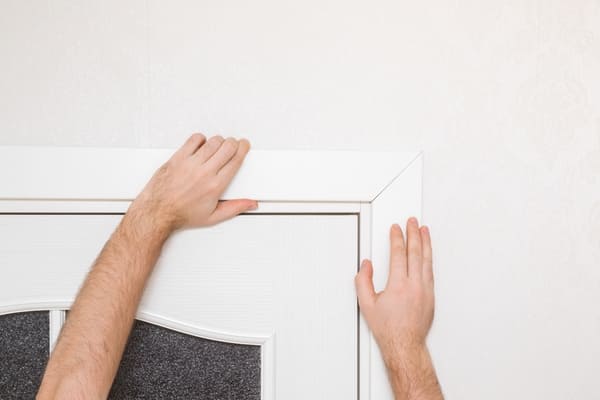 Zwei Hände greifen um Zarge einer hochwertigen weißen Innentür, in der rechten oberen Ecke, Montage von Innentüren rundum Dortmund
