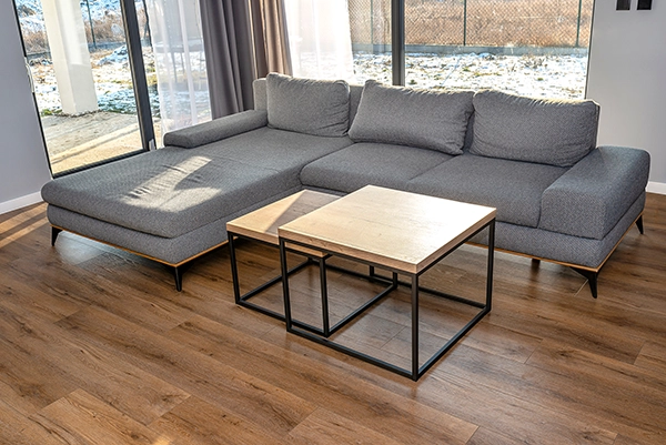 Vinyl in Essen - im gemütlichen Wohnzimmer In einem gemütlichen Wohnzimmer in Essen ist ein hochwertiger Vinylboden verlegt, im Raum steht eine graue Couch und zwei Couchtische
